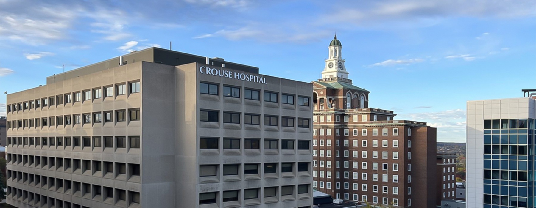 Landscape skyline photo of Crouse Hospital in the foreground of other Syracuse city skyline buildings