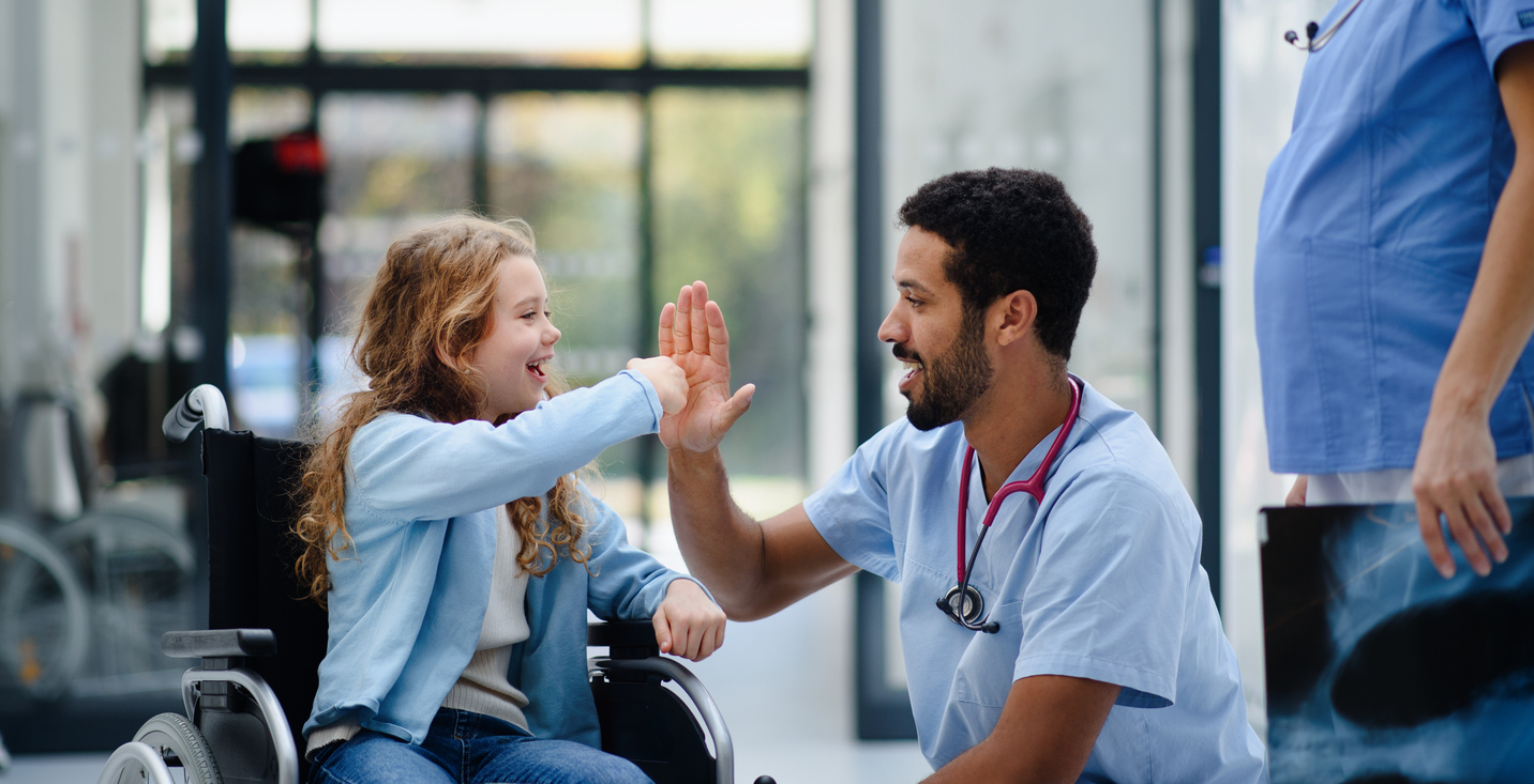 A young girl in a wheelchair high-fiving a male hospital worker.